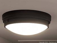 Close-up photo of the lit ceiling mount light showing black frame and white diffuser.