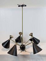 Showcases the entire mid century modern style Sputnik chandelier with 5 black conical lampshades and brass arms extending from the central spherical core. The brass rod and mounting plate are also visible.