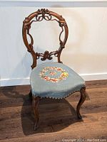 Full front view of vintage ladies chair showing ornate wooden backrest and floral needlepoint seat upholstery.