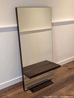 Front view of tall rectangular mirror with single dark wood shelf, showing overall design and condition.