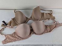 Two Victoria's Secret bras laid flat, one smooth nude bra and one nude with lace sides and band.