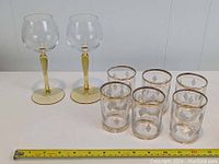 Two vintage stemmed glasses and six tumbler glasses with gold geometric patterns and yellow stems.