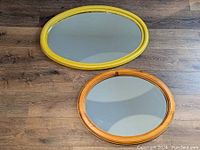 Two oval mirrors on wood floor, one yellow painted frame and one brown wood frame