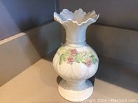 Front side view of white Belleek porcelain vase showing applied pink roses and green leaves, scalloped ruffled top edge and bulbous body.