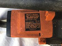 Close-up photo showing the product label with details: Black & Decker 12" Electric Chain Saw, model 1212, 115V, 60Hz, 2.2 amps.