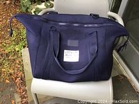 Front and top view of large dark blue neoprene carryall bag placed on a white chair outdoors.