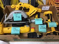 Photo of four DeWalt cordless tools arranged in a box showing model numbers on sticky notes: DC390 circular saw, DW960 angle drill driver, DW056 impact driver, and DCD760 drill driver. No batteries included.
