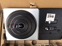 Front view of DJ Hero wireless turntable controller inside original packaging, showing colored buttons and turntable surface