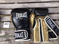 Pair of Everlast black and gold boxing gloves with visible logos on wrist strap and front, displayed on wood pallet surface