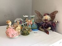 Collection of fairy figurines and glass globe music boxes on a shelf.