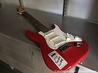 Red electric mini guitar laying on gray flooring. Visible body, neck, and headstock.