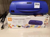 Blue GBC Creative Laminator sitting on its original box with power cord visible.