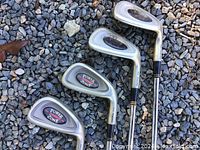 Four Dunlop Power Zone W iron golf clubs arranged on gravel; showing club heads with Power Zone logo