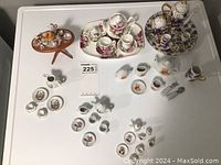 Overview of multiple miniature tea sets on white surface including floral sets and assorted small pieces