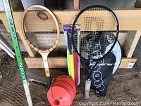 Two tennis rackets, one Wilson black and one vintage wooden, plastic cones, hockey stick, and racquet cover.
