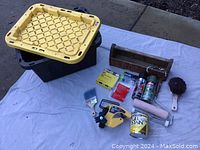 Overall view of paint supplies including storage bin, wooden toolbox, roller, brushes, spray paint, and hand masker.