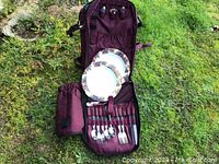 Maroon insulated wine backpack fully opened showing plastic plates and metal utensils inside the backpack.
