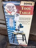Photo of the original packaging box showing Shop Fox branding, tool table model D2056, butcher block finish tabletop size 13x23 inches, and features of flared legs and adjustable feet.