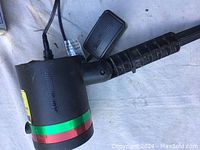 Close-up photo of the Star Shinemotion laser light showing the black handle, colorful bands, and power plug.