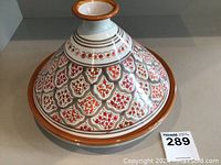 Top and side view of the hand-painted Moroccan ceramic tagine pot showing detailed painted pattern of scales in red and brown with a terracotta rim.