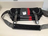 Front view of Timbuk2 messenger bag in black, gray, and red with flap closed and shoulder strap visible
