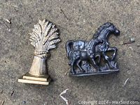 Both doorstops shown side by side on the ground, highlighting the horse with colt and wheat sheaf motifs.