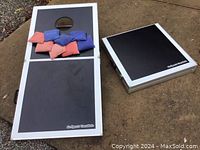 Two cornhole boards shown on the ground, one folded and one open with bean bags arranged on the board. Bean bags are red and blue.