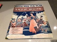 Sheet music cover titled 'Whistle While You Work' featuring Snow White and the Seven Dwarfs.