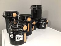 Black ceramic stoneware canisters with latch lids and wooden spoons attached