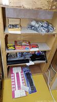 Shelf containing wood carving set in wooden box, staple gun with multiple packs of staples, black plastic flooring slides, and various metal brackets
