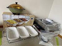 Photo showing three section white ceramic buffet server with its box and additional chafing dishes and a vintage bun warmer in background.