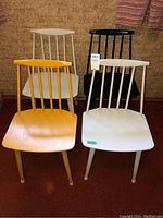 Four painted wood chairs (yellow, two white, black) with spindle backs.