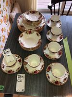 Full view of the collection of Aynsley china on table, showing plates, bowls, teacups, and saucers arranged in stacks and groups.