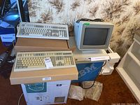 Two beige AT-style keyboards stacked on cardboard box with IBM CPU and monitor visible behind