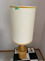 Full view of the lamp with white cylindrical shade with yellow trim and mustard yellow ceramic base.