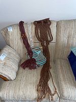 Full view of two macrame plant holders and macrame owl wall hanging laid on a beige fabric couch with a clothespin bag