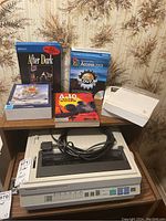 Overall photo showing the Panasonic printer on a wooden surface with power cable, four boxed computer games, and one Microsoft Office 2003 Access book.