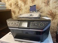 Front view of Epson Stylus Photo RX680 all-in-one printer with control panel and display screen. Accessories and box visible on top.