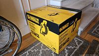 Front and side view of original yellow and black DeWalt cardboard box on floor near stairs