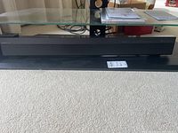 Full view of black Panasonic sound bar on carpet under glass table.