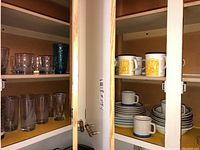 Photo of plastic cabinet shelves containing stacked plates, mugs with lemon design, and clear glass tumblers