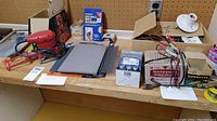 Wide view of lot showing red Power Max finishing sander, sandpaper sheets, boxed solder, small light, and other electrical components on wooden counter.
