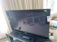 Panasonic 42-inch plasma TV on stand with remote control resting on stand shelf.
