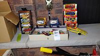 Overview of boxed Matchbox cars, Tonka trucks, other toy cars, and a yellow plastic car carrier trailer arranged on a stone hearth.