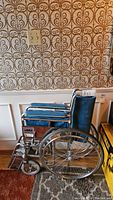 Side view of Lumex manual wheelchair showing blue fabric seat, armrests, metal frame, and large rear wheels with spokes.