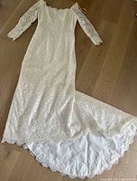 Full view of the entire wedding gown laid flat showing off-the-shoulder neckline, long lace sleeves, and the length of the skirt with train.