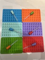 Photo showing six rectangular silicone gummy bear molds in different colors, each with matching colored droppers attached.