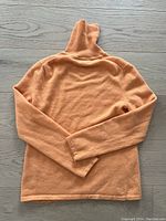Back view of orange cashmere sweater with long sleeves laid flat on wood floor