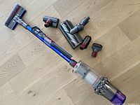 Assembled Dyson V11 vacuum with wand, dust bin and five attachments arranged on wood floor