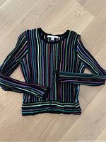 Front view of multicolor striped sweater laid flat showing ribbed neckline and hem with long sleeves.
